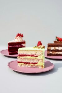 A selection of elegant gourmet cakes with diverse toppings on pastel pink plates, perfect for celebrations.